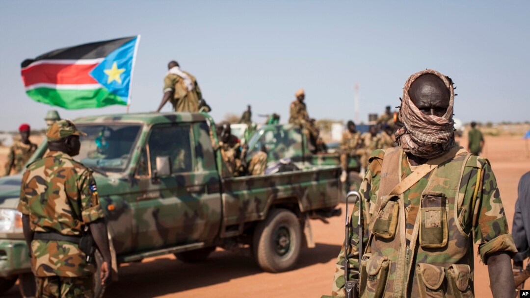 A South Sudanese government soldier stands with others near their vehicles, after government forces on Friday retook from rebel forces the provincial capital of Bentiu, in Unity State, South Sudan, Sunday, Jan 12, 2014.