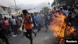 A protester playing two vuvuzelas walks next to a fire lighted for a ceremony during a demonstration against the government in Port-au-Prince, Haiti, Jan. 25, 2016. 