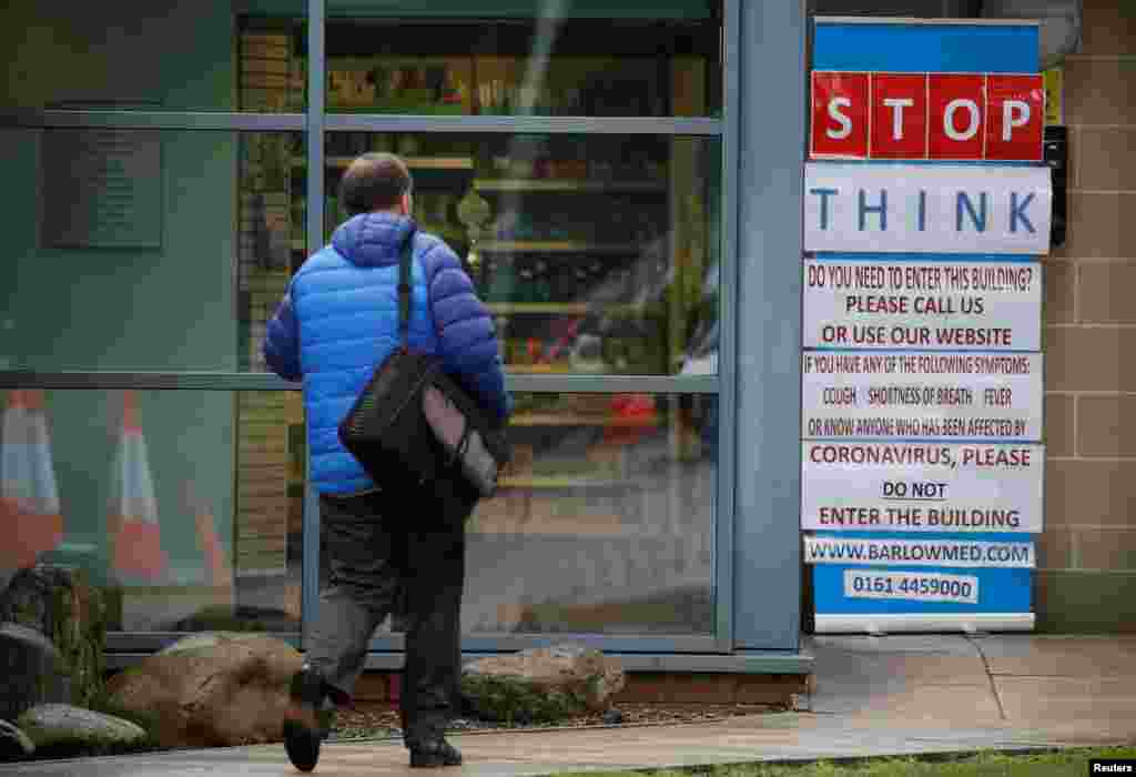 A man walks toward a coronavirus warning sign outside a medical center in Manchester, Britain.