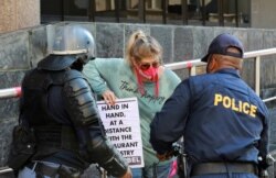 FILE - Police warn a demonstrator working in the hospitality industry during a protest against lockdown regulations in the streets close to Parliament in Cape Town, South Africa, July 24, 2020.