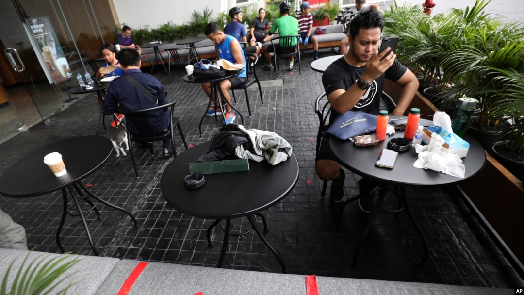 Para pengunjung sebuah kafe di Gelora Bung Karno duduk dalam jarak tertentu dalam upaya mencegah penyebaran virus corona, Jakarta, 26 Maret 2020. (Foto: Dita Alangkara/AP)