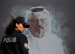 FILE - A Turkish police officer walks past a picture of slain Saudi journalist Jamal Khashoggi prior to a ceremony, near the Saudi Arabia Consulate in Istanbul, marking the one-year anniversary of his death, Oct. 2, 2019.