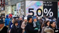 Crowds walk past a large store sign displaying a Black Friday discount in midtown Manhattan, Nov. 23, 2018, in New York. 