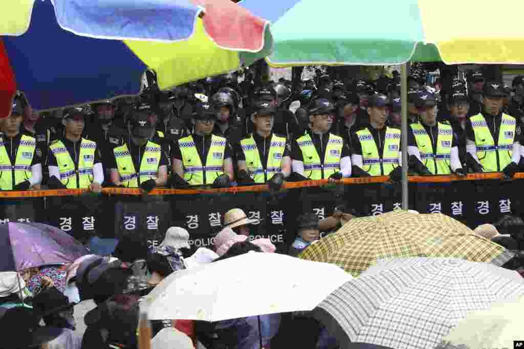 Evangelical Baptist Church believers sit as police officers searching for a fugitive billionaire businessman over April's ferry sinking stand in line in font of the main gate of the church in Anseong, South Korea, June 11, 2014. 