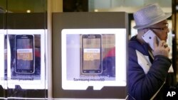 FILE - A man uses an Apple iPhone as he passes a Samsung shop in Seoul, South Korea, Jan. 29, 2015.