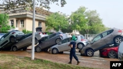 Warga berjalan di dekat mobil-mobil yang menumpuk akibat banjir di Picanya, dekat Valencia, Spanyol timur, pada 30 Oktober 2024. (Foto: AFP)