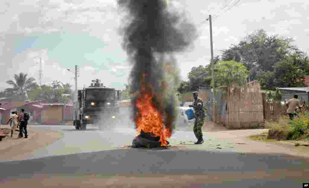 Un soldat de l'armée burundaise, avec un seau d'eau, tente d'éteindre le feu d'un pneu brulé par les manifestants dans la capitale Bujumbura, Burundi, lundi 27 avril 2015.