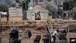FILE - Two Palestinian boys stand outside a tent, background, watching workers rebuild a house which was destroyed during the 2014 summer war between Israel and Hamas, as the long-awaited reconstruction began in Shijaiyah neighborhood eastern Gaza City, July 23, 2015.