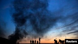 Kurdish refugees walk on a hilltop as thick smoke rises from Syrian town of Kobani during heavy fighting between Islamic State and Kurdish Peshmerga forces, seen from the Turkish-Syrian border in Suruc, Turkey, Oct. 26, 2014.