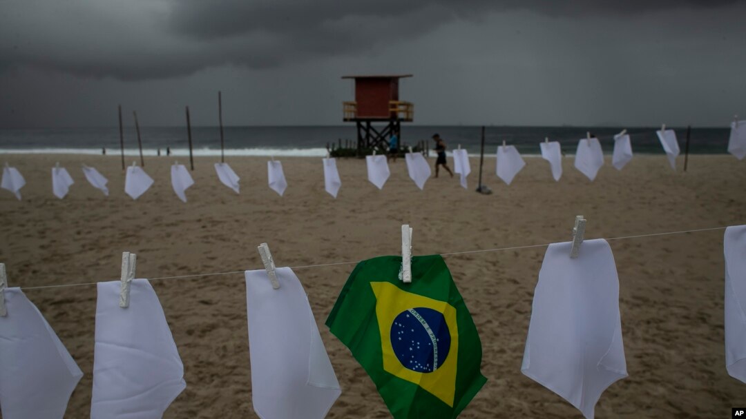 Una bandera brasileña cuelga de un tendedero en la playa de Copacabana en medio de pañuelos blancos que representan a los que han fallecido a causa del COVID-19, en Río de Janeiro, Brasil, el viernes 8 de octubre de 2021. 