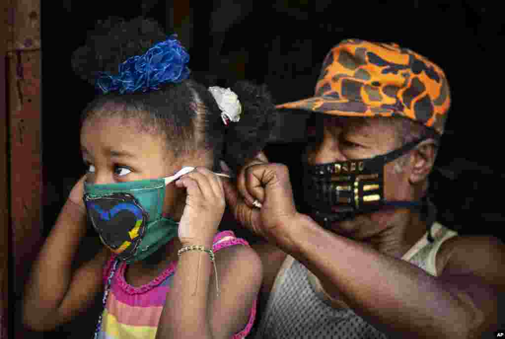 Andrés Jiménez, de 69 años, un trabajador estatal retirado que hace máscaras para vender en su vecindario, ata una máscara a una niña, como precaución contra la propagación del nuevo coronavirus en La Habana, Cuba. Las autoridades cubanas han ordenado el uso de máscaras para cualquier persona que salga fuera de sus hogares.