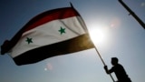 A Syrian protester stands on top of a building as he waves a Syrian flag, during a demonstration against a U.S. raid at a village near the Syrian-Iraqi border, in Damascus, Syria, Oct. 30, 2008. Hundreds of Syrian riot police ringed the shuttered and clos