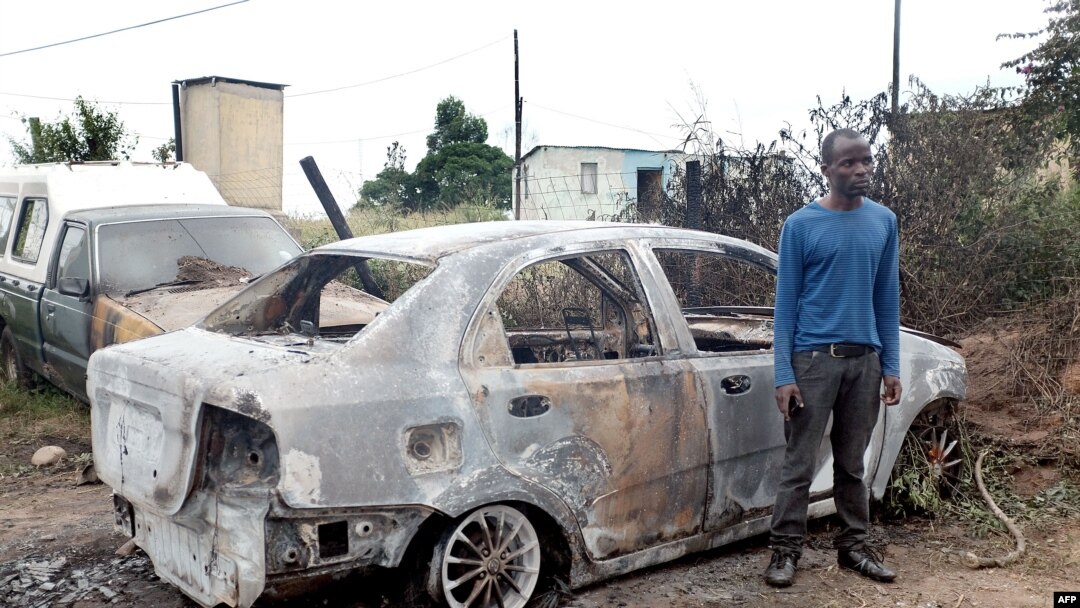 In this April 19, 2015, photo a foreign national from Zimbabwe stands by one of his two cars set alight after he survived a petrol bomb attack at his home in Illovo, some 55 kilometers south of Durban, South Africa. Tensions are high in South Africa’s capital, Feb. 20, 2017, amid a wave of attacks against businesses owned by immigrants.