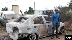 In this April 19, 2015, photo a foreign national from Zimbabwe stands by one of his two cars set alight after he survived a petrol bomb attack at his home in Illovo, some 55 kilometers south of Durban, South Africa. Tensions are high in South Africa’s capital, Feb. 20, 2017, amid a wave of attacks against businesses owned by immigrants.