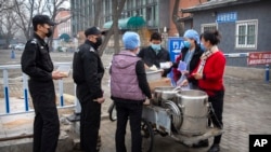 Security guards line up as workers in face masks dispense lunch outside of an office building in Beijing, Feb. 21, 2020.