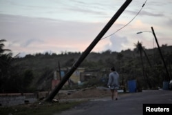 A woman walks under a partially collapsed utility pole in Maunabo, Jan. 27, 2018.