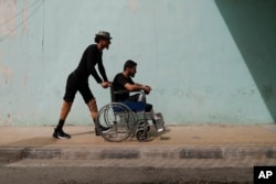 In this Oct. 7, 2018, photo, a Syrian soldier who lost his legs while fighting in Syria's war, helps his comrade after a physical therapy session, at the Ahmad Hamish Martyr hospital in Damascus, Syria.