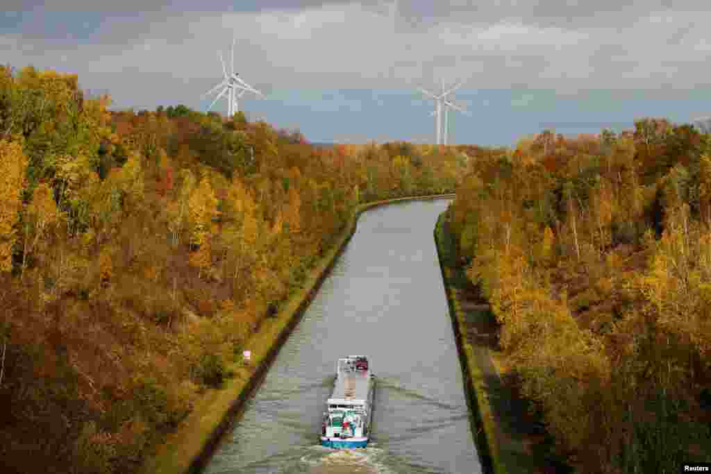 A river barge navigates on the canal saA river barge navigates though the canal surrounded by golden, green and rust-colored autumnal leaves in Havrincourt, France.urrounded by golden, green and rusty leaves color of the autumn in Havrincourt, France.