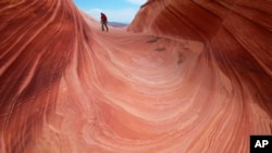 FILE - In this May 28, 2013, photo, a hiker walks on a rock formation known as The Wave in the Vermilion Cliffs National Monument in Arizona.
