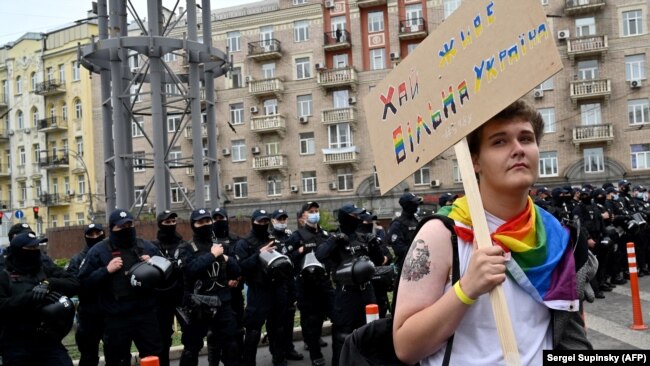 Seorang aktivis LGBTQ tampak berdiri di dekat rombongan polisi yang mengawal aksi pawai Pride di ibu kota Ukraina, Kiev, pada 19 September 2021 (Foto: AFP/Sergei Supinsky)