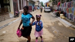 FILE - A child sips on a refreshment as she is walked home from school, in Cap-Haitien, Haiti, April 17, 2024. 