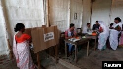 A woman (L) casts her vote with an electronic voting machine as others get their voting slip from an officer at a polling station in Majuli, a large river island in the Brahmaputra river, Jorhat district, in the northeastern Indian state of Assam, April 7