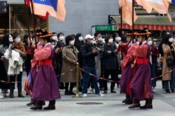 Warga mengenakan masker saat menyaksikan upacara peragaan pergantian Pengawal Kerajaan, di depan gerbang utama Istana Deoksu di Seoul, Korea Selatan, Jumat, 13 November 2020.