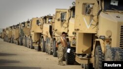 FILE - A contractor walks between trucks returned from Iraq to Camp Arafjan in Kuwait December 16, 2011. Vehicles which return from Iraq are scrapped or repaired, cleaned and shipped to Afghanistan or returned to the United States.