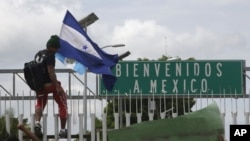 Un migrante hondureño sostiene su bandera y sube a la valla en Ciudad Hidalgo, México. Octubre 18, 2018.