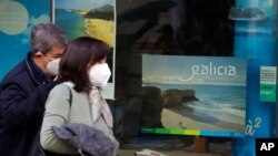 FILE - A couple wearing face masks to protect against the spread of coronavirus walk past a closed travel agency in Madrid, Spain, March 22, 2021. Some EU countries are throwing their support behind so-called vaccine passports.