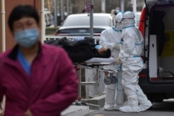 FILE - Medical workers wearing protective suits as a precaution against the coronavirus deliver a patient to the fever clinic at a hospital in Beijing, Jan. 13, 2021.