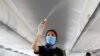 FILE - A flight attendant wearing a face mask sprays disinfectant inside a plane at Sharm el-Sheikh International Airport, Egypt, June 20, 2020.