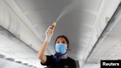 FILE - A flight attendant wearing a face mask sprays disinfectant inside a plane at Sharm el-Sheikh International Airport, Egypt, June 20, 2020.