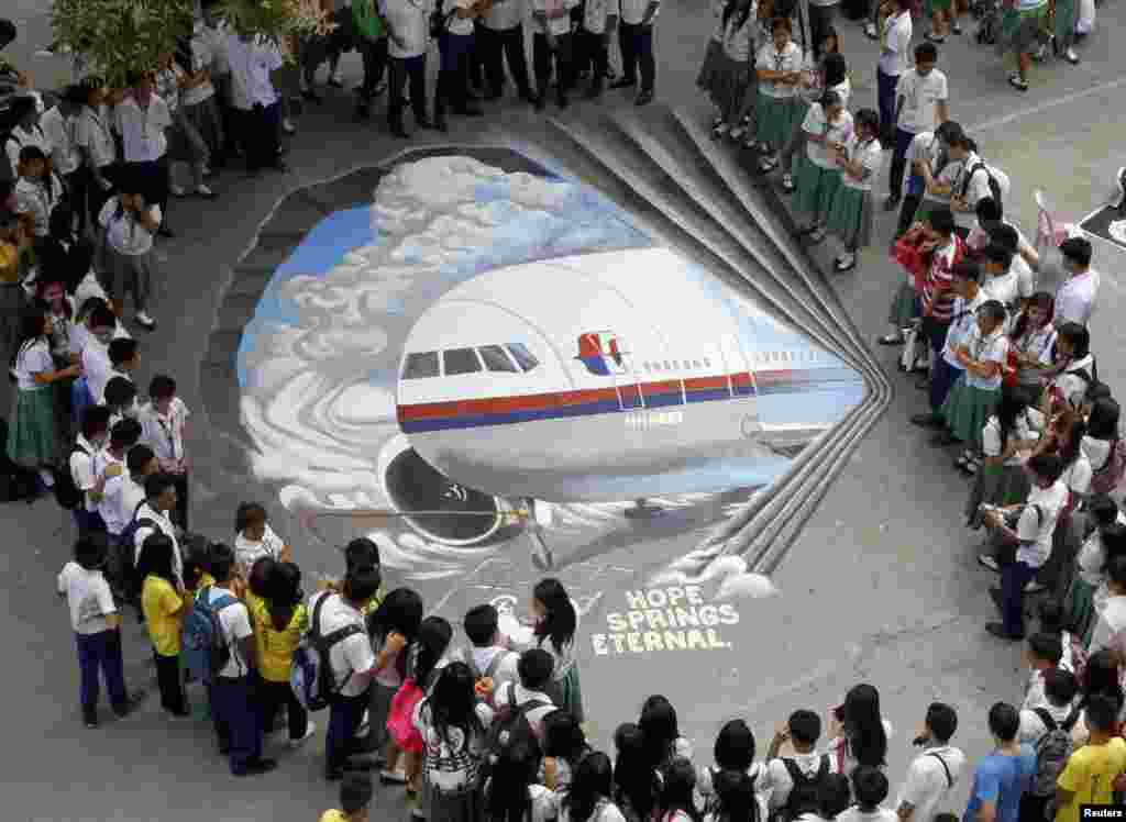 Sinh viên đứng vây quanh một tác phẩm nghệ thuật 3 chiều, dựa trên chuyến bay mất tích MH370 của hãng hàng không Malaysia Airlines, được vẽ trên sân trường ở thành phố Makati, Metro Manila, Philippines.