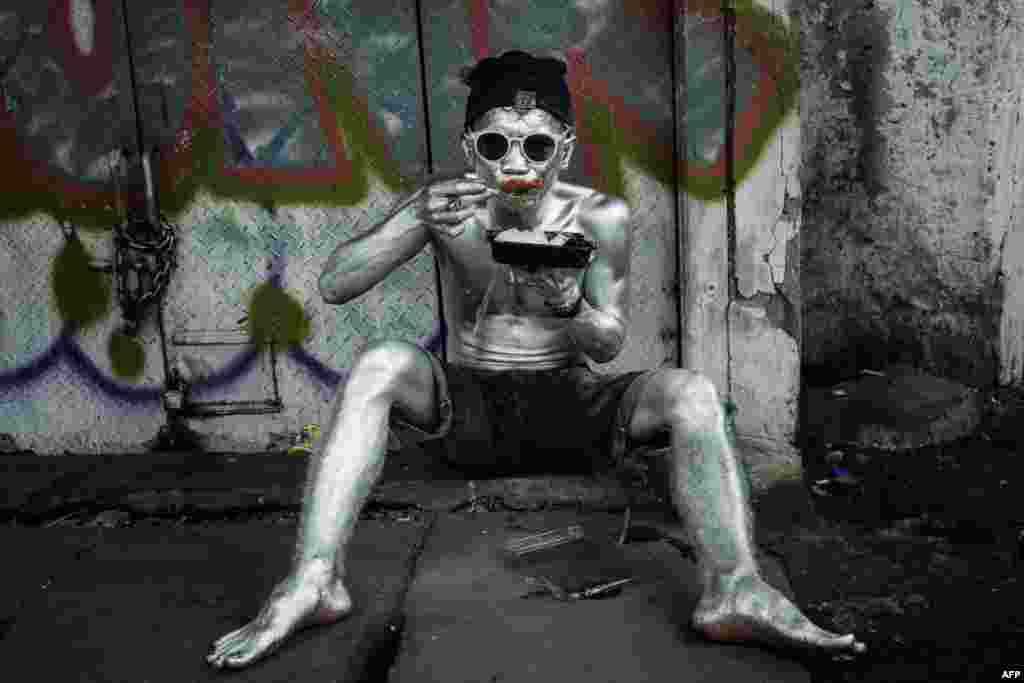 A street performer covered in silver paint takes a break to eat in Jakarta, Indonesia.