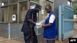 A police officer helps a worker to put on his gloves to protect himself from virus infection, July 31, 2012 at the Mulago Hospital in Kampala.