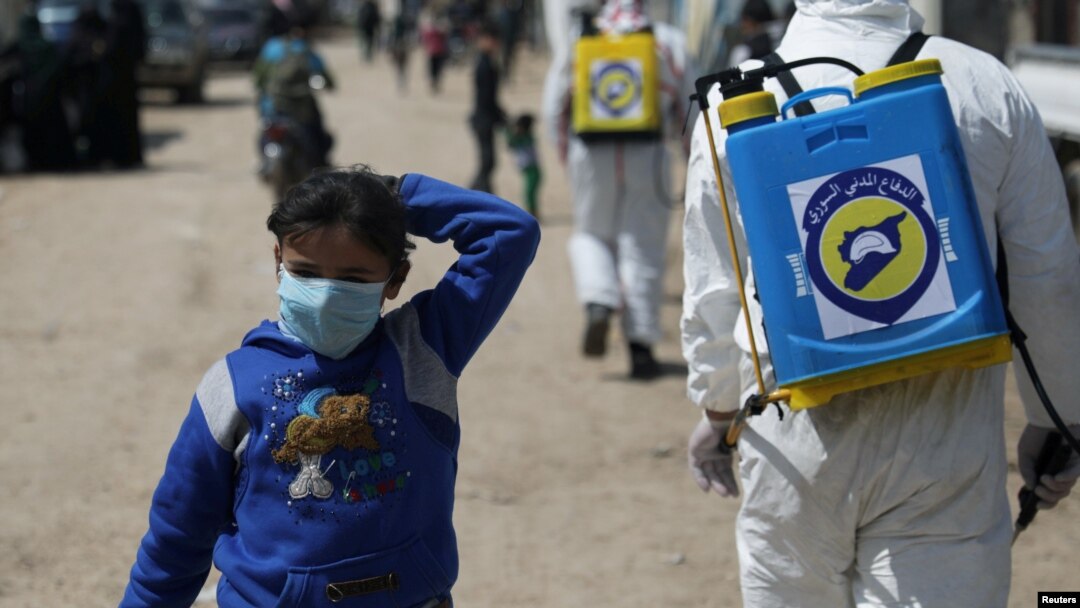 FILE - FILE - An internally displaced Syrian girl wears a face mask as members of the Syrian Civil defense sanitize the Bab Al-Nour internally displaced persons camp, to prevent the spread of coronavirus disease (COVID-19) in Azaz, Syria, March 26, 2020.