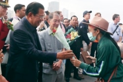 Cambodia's Prime Minister Hun Sen, left, gives a bouquet of flowers to a passenger who disembarked from the MS Westerdam, owned by Holland America Line, at the port of Sihanoukville, Cambodia, Friday, Feb. 14, 2020.