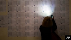 A woman uses the light of her cell phone to search for her name to vote, at a polling station during a parliamentary election in Yerevan, Armenia, April 2, 2017.