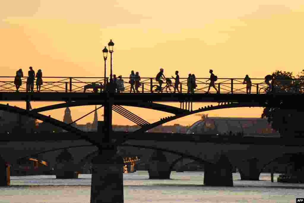 At sunset pedestrians and cyclists pass over The Art Bridge across the River Seine in Paris, France.