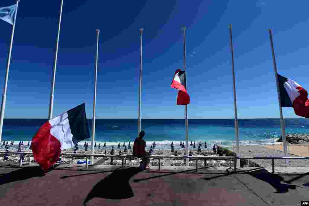 A woman sits under French flags lowered at half-mast in Nice, a day after the deadly Bastille Day attacks that killed at least 84 people.