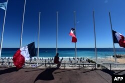 A woman sits under French flags lowered at half-mast in Nice on July 15, 2016, following the deadly Bastille Day attacks.