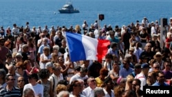 A French flag flies among the crowd as people gather in front of the Monument du Centenaire during a minute of silence on the third day of national mourning to pay tribute to victims of the truck attack along the Promenade des Anglais on Bastille Day that