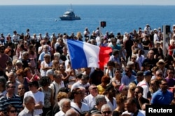 A French flag flies among the crowd as people gather in front of the Monument du Centenaire during a minute of silence on the third day of national mourning to pay tribute to victims of the truck attack along the Promenade des Anglais on Bastille Day that