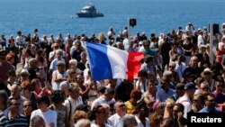 A French flag flies among the crowd as people gather in front of the Monument du Centenaire during a minute of silence on the third day of national mourning to pay tribute to victims of the truck attack along the Promenade des Anglais on Bastille Day that