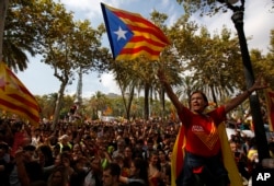 FILE - A woman gestures as others wave the ''estelada'' or Catalonia independence flags during a protest in Barcelona, Spain, Sept. 21, 2017.