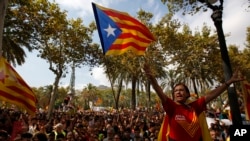 FILE - A woman gestures as others wave the ''estelada'' or Catalonia independence flags during a protest in Barcelona, Spain, Sept. 21, 2017.