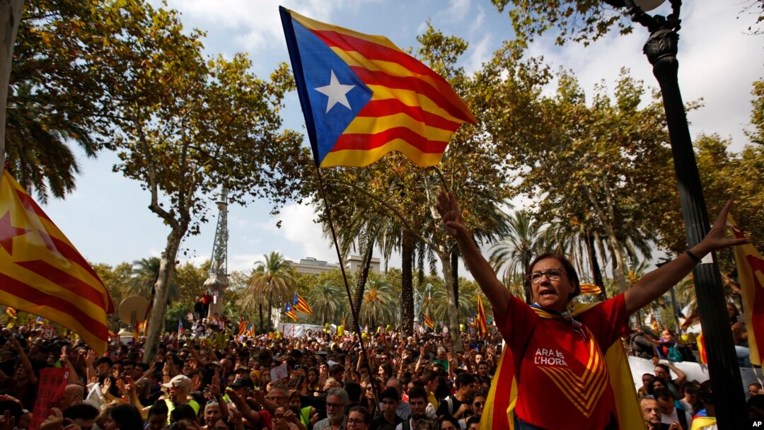FILE - A woman gestures as others wave the ''estelada'' or Catalonia independence flags during a protest in Barcelona, Spain, Sept. 21, 2017.