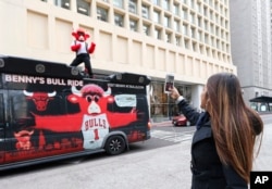 FILE - Chicago Bulls' mascot Benny the Bull is photographed by a pedestrian as he reenacts the famous scene of Ferris Bueller singing during a parade at Daley Plaza while shooting a daylong Snapchat video.