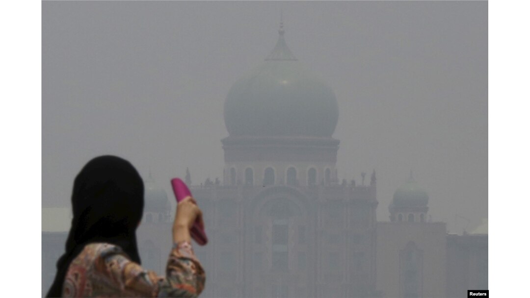 FILE - A woman looks toward the Malaysian prime minister's office in Putrajaya, which is shrouded in haze from fires in Indonesia, Oct. 6, 2015.